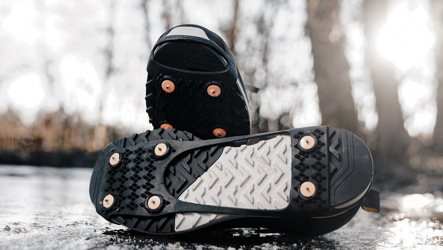 A pair of ice grippers on hiking shoes lying on a frosty road