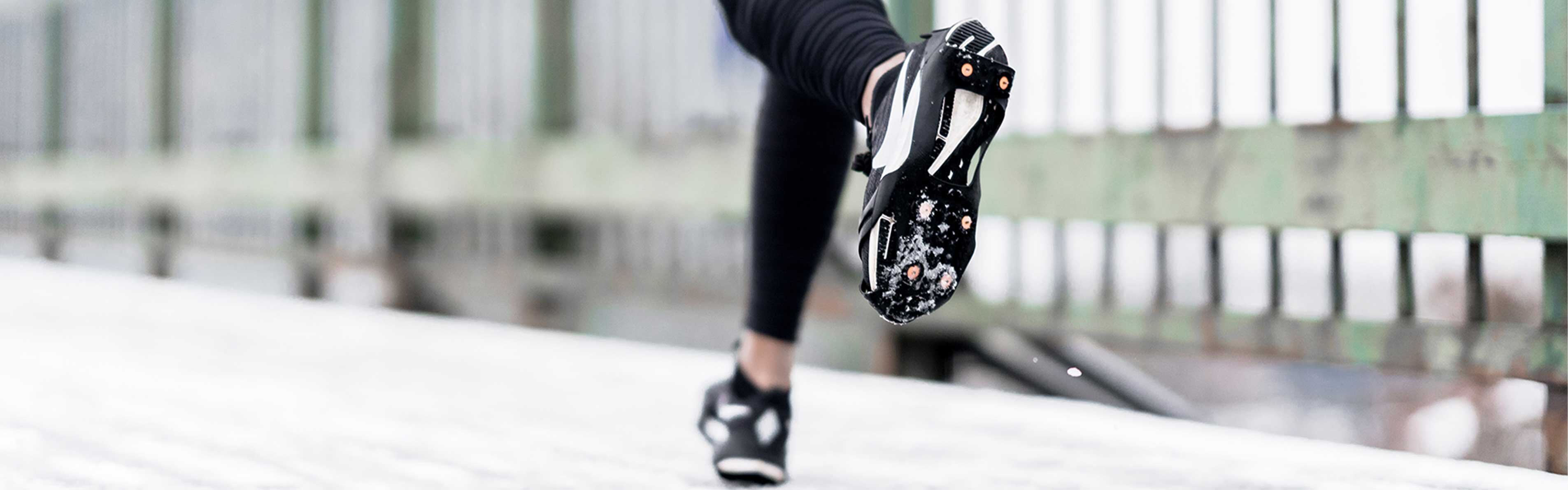 Close-up of a runner on a frosty city road, wearing shoes with ice grippers for traction.