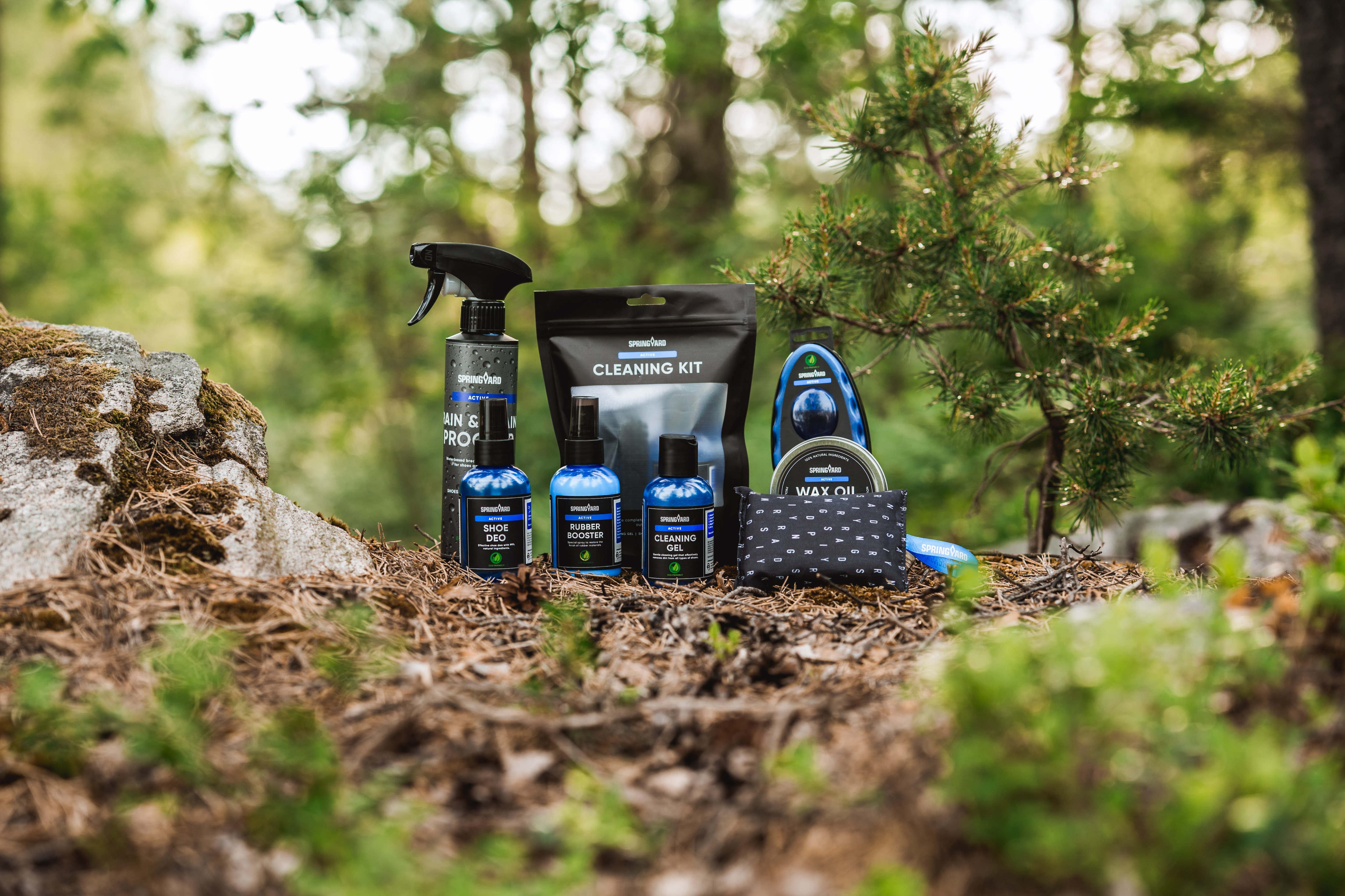 Åtta olika produkter från Springyards Active-serie placerade i en naturlig skogsmiljö med barr, kottar och stenar.